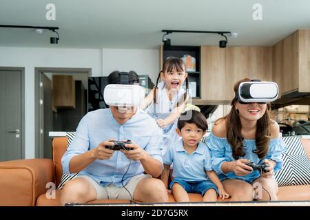 Glückliche asiatische Familie zu Hause auf Wohnzimmer Sofa mit Spaß, während sie aussehen Mutter und Vater spielen Mit Virtual Reality Headset VR in l Stockfoto