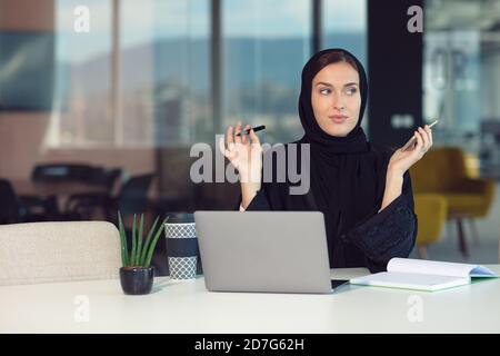 Nachdenkliche arabische Geschäftsfrau, die am Arbeitsplatz im Büro sitzt Stockfoto