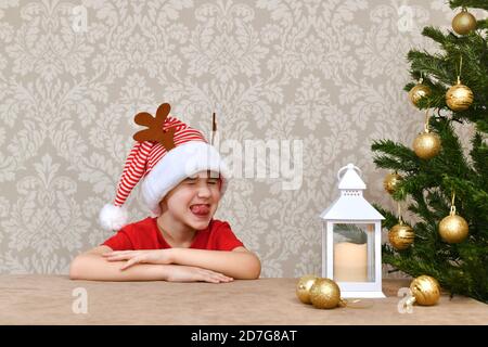 Ein Junge in einem Karneval gestreifte rot-weiße Mütze mit Hirschhörnern schloss seine Augen und machte ein fröhliches Gesicht. Stockfoto
