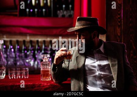 Mann mit Bart hält ein Glas Brandy. Verkostung und Degustation. Bärtiger Kerl im Retro-Anzug mit Glas Whiskey. Teure Getränke. Vintage Barkeeper mit Stockfoto