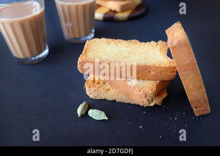 Tea Time Snack - gesunde Weizen Zwieback serviert mit indischen heißen Masala Tee, auf schwarzem Hintergrund mit dem Kardamom. Auch bekannt als Mumbai Cutting Chai. Stockfoto