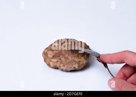 Hand hält eine Gabel über gekochten Fleisch Patty auf einem weißen Teller isoliert auf weißem Hintergrund, Nahaufnahme, Kopierraum Stockfoto