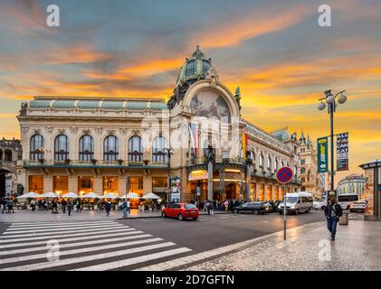 Die Sonne untergeht in der Neustadt Prag, Tschechische Republik, während die Einheimischen die Hauptstraße vor dem Prager Gemeindehaus durchqueren. Stockfoto