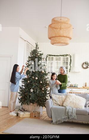 Zwei Schwestern zusammen mit ihrer Mutter schmücken Weihnachtsbaum in Das Wohnzimmer bereiten sie für den Urlaub Stockfoto