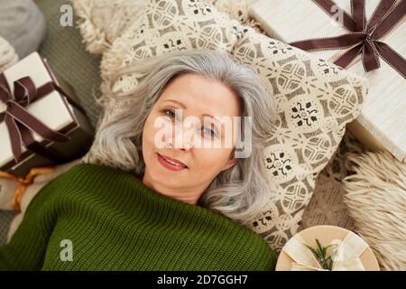 High-Angle-Ansicht der reifen Frau auf Kissen unter liegen Geschenke, die sich ausruhen und die Kamera betrachten Stockfoto