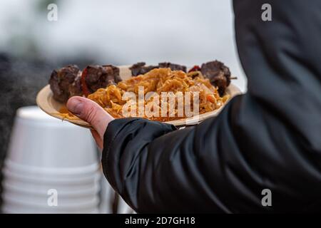 Gedünstetes Kohl mit Würstchen - ein traditionelles Gericht auf dem jährlichen Weihnachtsmarkt, Hände halten einen Teller mit warmen Speisen, Nahaufnahme, weicher Fokus Stockfoto