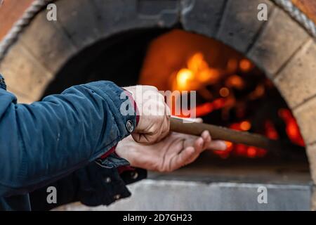 Hände eines Pizzaherstellers, der Pizza mit einer Schaufel, Nahaufnahme, Weichfokus in den Ofen stellt Stockfoto