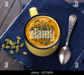 Kürbissuppe mit Kürbiskernen und Thymian im Becher Auf einer hölzernen Oberfläche Stockfoto