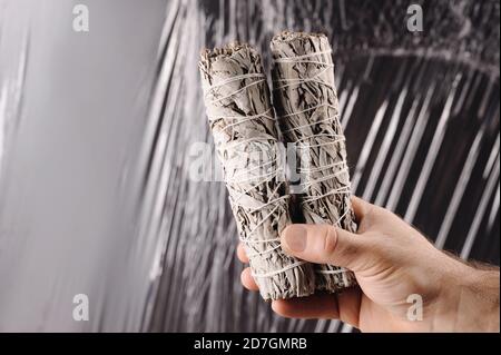 Hand hält einen weißen Salbei widge Sticks auf dem grauen Hintergrund. Brennender Weihrauch mit weißem Salbei. Stockfoto