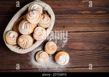 Köstliche moderne Cruffins werden aus geschichteten Croissants in Form eines Muffins. Cruffins mit einem Holzkorb auf dunklem Hintergrund, mit einem besprengten Witz Stockfoto