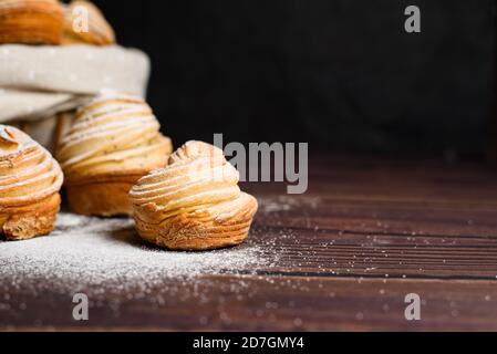 Köstliche moderne Cruffins werden aus geschichteten Croissants in Form eines Muffins. Cruffins mit einem Holzkorb auf dunklem Hintergrund, mit einem besprengten Witz Stockfoto