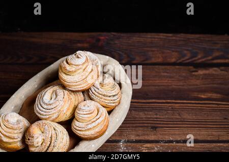 Leckere moderne Cruffins werden aus Puffhörnchen in Form eines Muffins hergestellt. Cruffins mit einem Holzkorb auf dunklem Holzhintergrund, bestreut Stockfoto