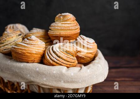 Köstliche moderne Cruffins werden aus geschichteten Croissants in Form eines Muffins. Cruffins mit einem Holzkorb auf dunklem Hintergrund, mit einem besprengten Witz Stockfoto