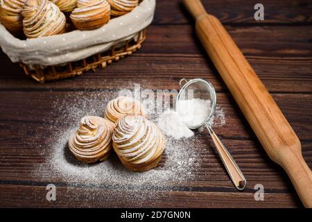 Moderne Cruffins werden aus Blättercroissants in Form eines Muffins hergestellt. In einem Holzkorb auf dunklem Grund, bestreut mit Puderzucker. Kopie sp Stockfoto