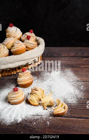 Leckere moderne Cruffins werden aus Puffhörnchen in Form eines Muffins hergestellt. Cruffins mit einem Holzkorb auf dunklem Holzhintergrund, bestreut Stockfoto