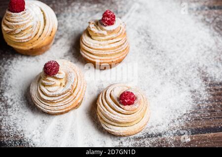 Leckere Cruffins werden aus mehrschichtigen Croissants in Form eines Bun hergestellt. Muffins auf dunklem Holzgrund, bestreut mit Puderzucker und Raspel Stockfoto