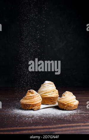 Moderne Mode Gebäck in 2020-cruffins, eine Mischung aus Croissants und Muffins. Drei cruffins auf einem dunklen Tisch mit Puderzucker bestreut Stockfoto