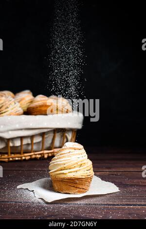 Moderne, modische Backwaren - Cruffins, Puffmuffin, eine Mischung aus Croissants und Muffins. Auf einem dunklen Holztisch mit Puderzucker bestreut. Ort t Stockfoto