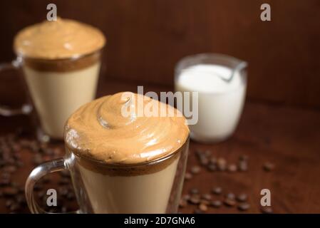 Kalter Dalgon-Kaffee in klaren Gläsern auf dunklem Holzhintergrund. Schaum aus Zucker und Instantkaffee wird mit einem Mixer über kalte Milch geschlagen. Koreanisch und Stockfoto