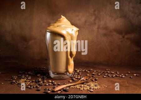 Kalter Dalgona-Kaffee in klaren Gläsern auf dunklem Holzhintergrund. Schaum aus Zucker und Instant-Kaffee mit einem Mixer auf kalter Milch peitscht. Nahaufnahme Stockfoto