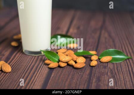 Mandelmilch in einem Glas auf einem Holzhintergrund. Nahaufnahme von Mandelkernen und grünen Blättern neben dem Glas. Stockfoto