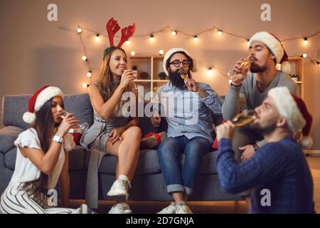 Gruppe von jungen Freunden trinken Champagner auf dem Sofa sitzen und Boden während der Weihnachtsfeier zu Hause Stockfoto