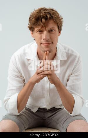 Gut aussehend lächelt berühren mit Zeigefinger seines Kinns. Porträt von niedlichen rothaarigen Kerl in weißem Hemd Stockfoto