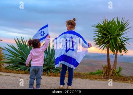 Zwei patriotische jüdische kleine Mädchen stehen und genießen mit der Flagge Israels auf Naturhintergrund. Stockfoto