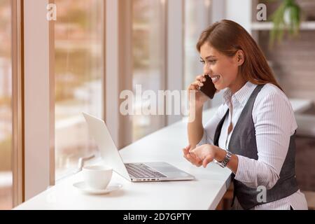Eine junge Frau mit Computer und Smartphone in Innenräumen, arbeitet im Büro. Stockfoto