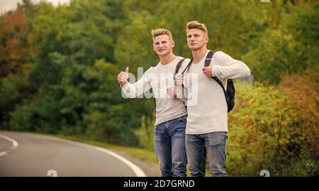 Anhalter und Auto mit Daumen hoch Geste auf dem Land. Unterwegs. Genießen Sie die Sommerwanderung. Auf der Suche nach Transport. Zwillinge zu Fuß entlang der Straße. Auto mit Daumen nach oben Geste stoppen. Stockfoto