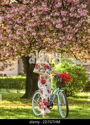 Frühlingsferien. Frau mit Tulpenstrauß. Sakura Baum blüht. Sakura-Saison. Romantische Fahrradtour. Tourismuskonzept. Transport und Reisen. Mädchen langes Kleid retro Cruiser Fahrrad Sakura Baum. Stockfoto