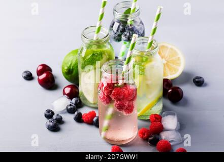 Beeren, Früchte und Zitrusfrüchte alkoholfreie kalte Getränke und Cocktails in Glasflaschen auf blauem Hintergrund, Kopierraum Stockfoto