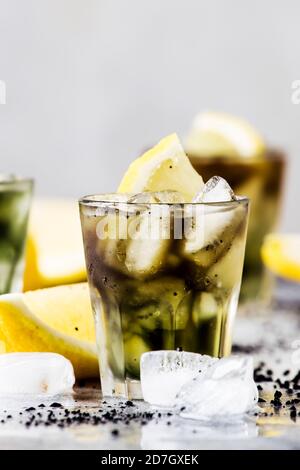 Gesundes Essen und Trinken Konzept: eistickes schwarzes Detox-Limonadenwasser mit zerkleinerten Eis- und Zitronenscheiben in Gläsern, Aktivkohle, grauer Hintergrund, tre Stockfoto