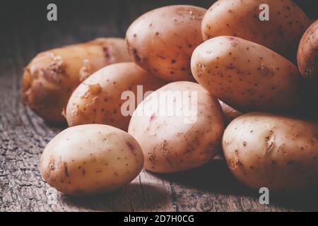 Frische Frühlingskartoffeln mit Gewürzen auf dem alten Holzhintergrund im rustikalen Stil, selektiver Fokus und getöntes Bild Stockfoto