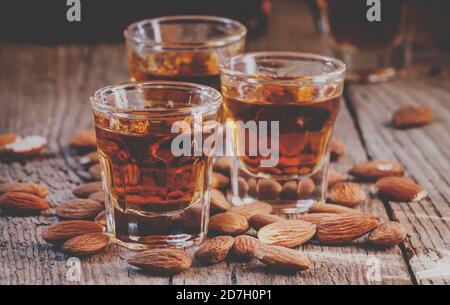 Italienischer Amaretto Likör mit trockenen Mandeln auf dem alten Holzhintergrund, selektiver Fokus und getöntes Bild Stockfoto