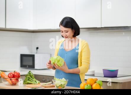 Gerne schwangere Frau zu Hause kochen, frischer Salat, essen viele verschiedene Gemüse während der Schwangerschaft, gesunde Schwangerschaft Konzept Stockfoto