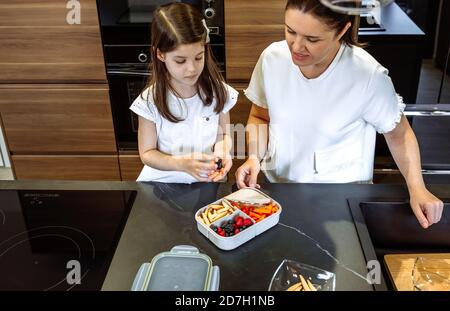 Mutter beobachtete, wie ihre Tochter Essen in ihre Lunchbox legte Stockfoto