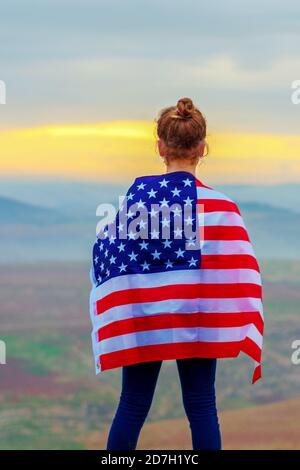 Junge kleine Mädchen hält Flagge von Amerika USA bei Sonnenuntergang im Freien. Stockfoto