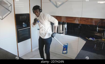 Happy Handsome schwarzen Mann hört die Musik und mit Besen als Gitarre. Aufräumen Wohnung. Hochwertige Fotos Stockfoto