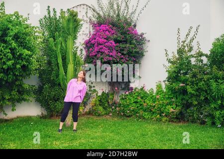 Frau und ein Baum mit violetten Blumen. Die Frau auf dem Rasen neben dem Kaktus. Stockfoto