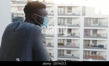 Einsamer schwarzer Mann mit medizinischer Maske auf dem Balkon. Quarantäne und psychische Probleme. Hochwertige 4k-Aufnahmen Stockfoto