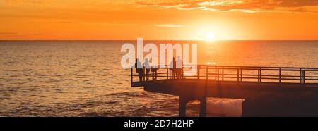 PERTH, AUSTRALIEN - 18. Jun 2020: Sonnenuntergang an der Küste, mit Menschen, die auf einem Pier silhouettiert stehen Stockfoto