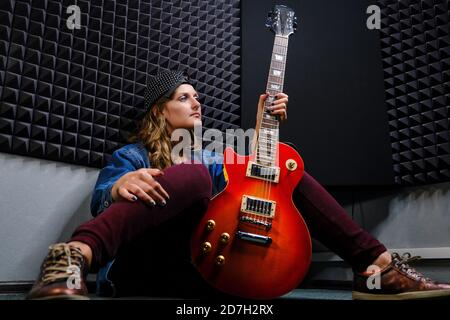 Musikerin Frau sitzt mit einer roten E-Gitarre in den Händen. Eine junge Frau Gitarrist in Jeans mit einer schönen Gitarre. Professionelle Aufnahme Studi Stockfoto