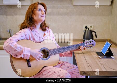 Eine junge Musikerin arbeitet von zu Hause aus. Eine Frau mit Gitarre führt online Unterricht durch. Stockfoto