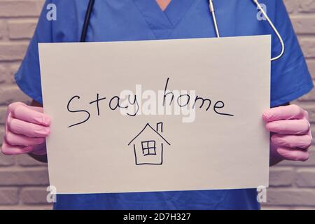 Eine Krankenschwester in Schutzhandschuhen hält ein Blatt Papier mit einer handschriftlichen Nachricht-Aufenthalt zu Hause. Arzt in einer medizinischen Uniform mit weißem Laken, Nahaufnahme Stockfoto