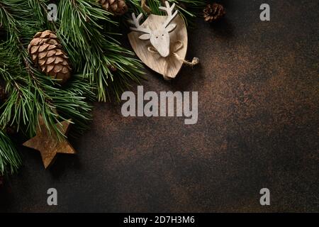 Weihnachtliche festliche Komposition mit Holzdekorationen und immergrünen Zweigen auf braunem Hintergrund mit Kopierraum. Grußkarte. Blick von oben. Stockfoto