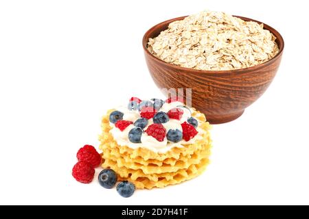 Frische Heidelbeeren, Himbeeren, Waffelplätzchen und Haferflocken in einer Schüssel mit einem Holzlöffel isoliert auf weißem Hintergrund. Stockfoto