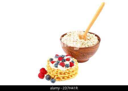 Frische Heidelbeeren, Himbeeren, Waffelplätzchen und Haferflocken in einer Schüssel mit einem Holzlöffel isoliert auf weißem Hintergrund. Stockfoto