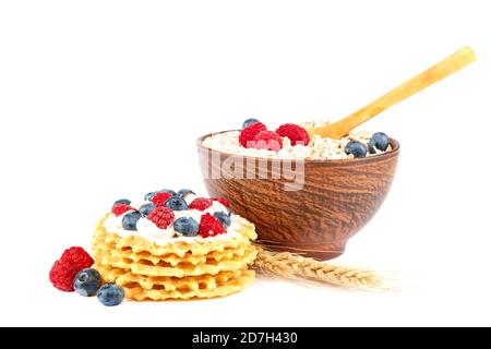 Frische Heidelbeeren, Himbeeren, Waffelplätzchen und Haferflocken in einer Schüssel mit einem Holzlöffel isoliert auf weißem Hintergrund. Stockfoto