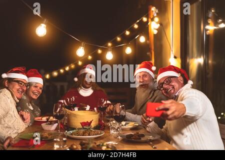 Glückliche ältere Freunde essen und feiern Weihnachtsferien während der Einnahme Selfie mit dem mobilen Smartphone auf der Terrasse des Hauses Stockfoto